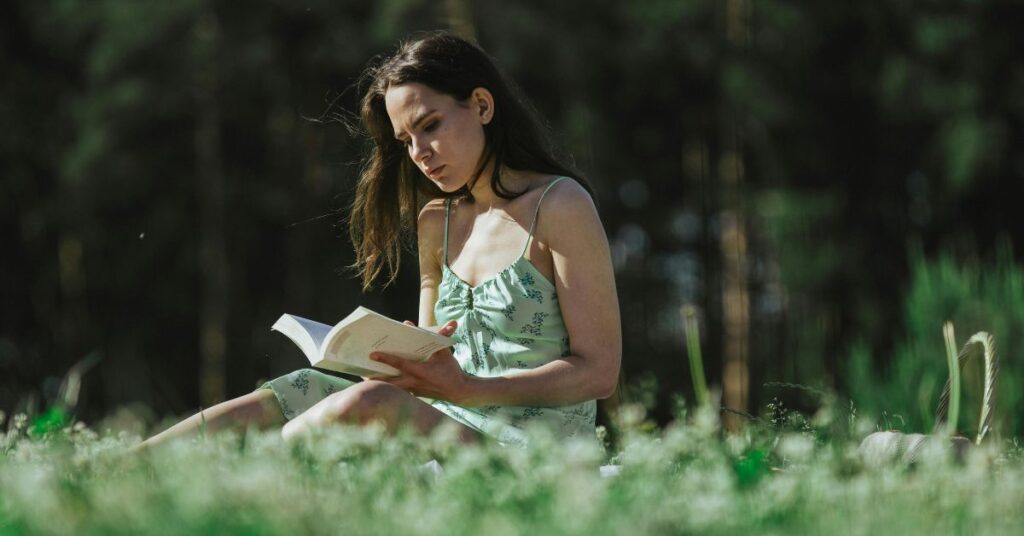 एक युवती शांत वातावरण में घास पर बैठकर पुस्तक पढ़ रही है, यह छवि अध्ययन और आत्मचिंतन का प्रतीक है।